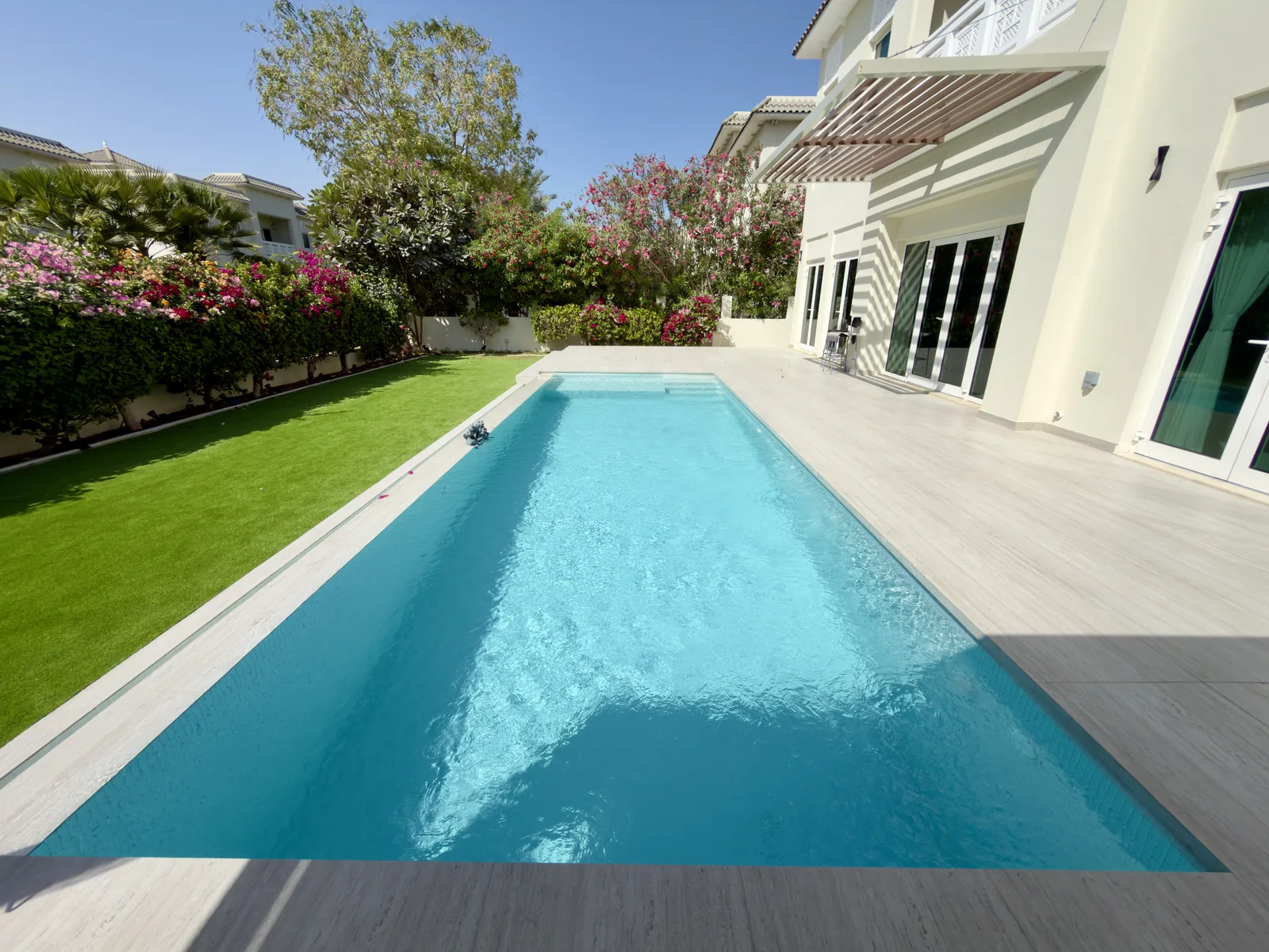 Long swimming pool beside a villa, lawn and flowering garden