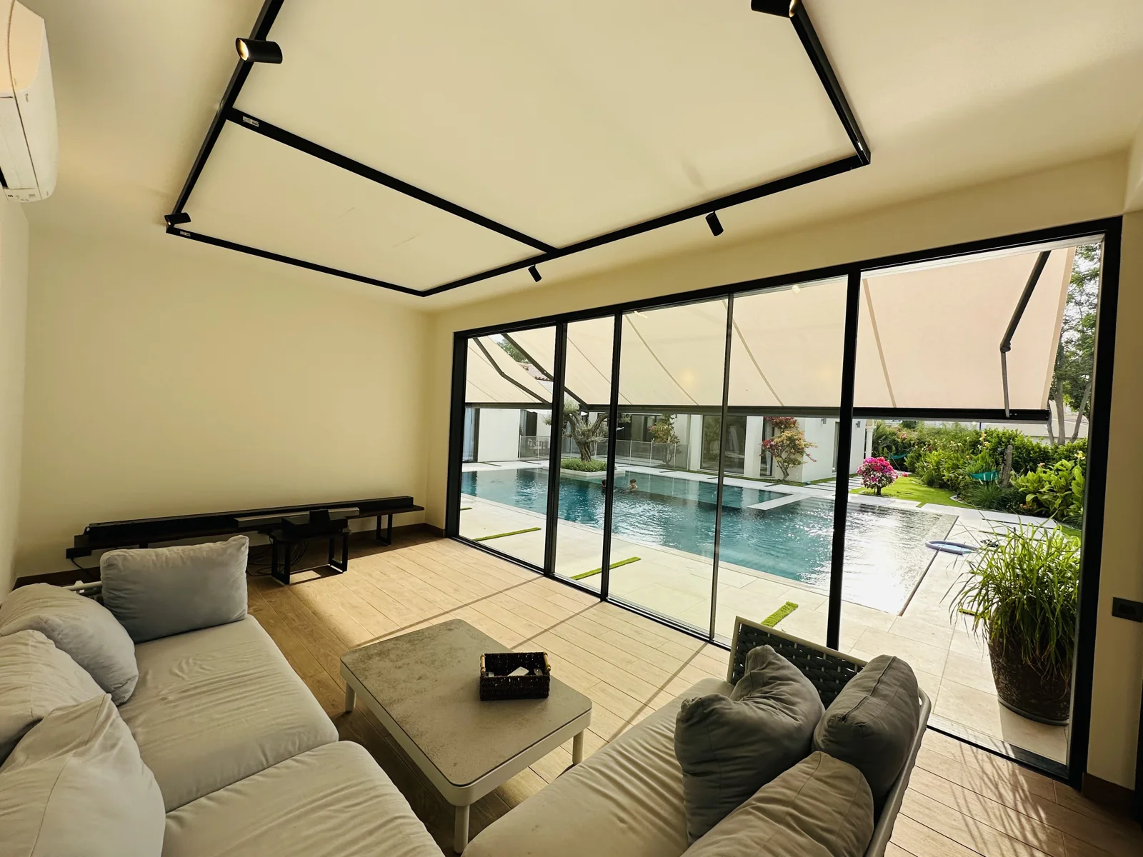Living room with grey seating, black framed glass doors and a view of the courtyard pool