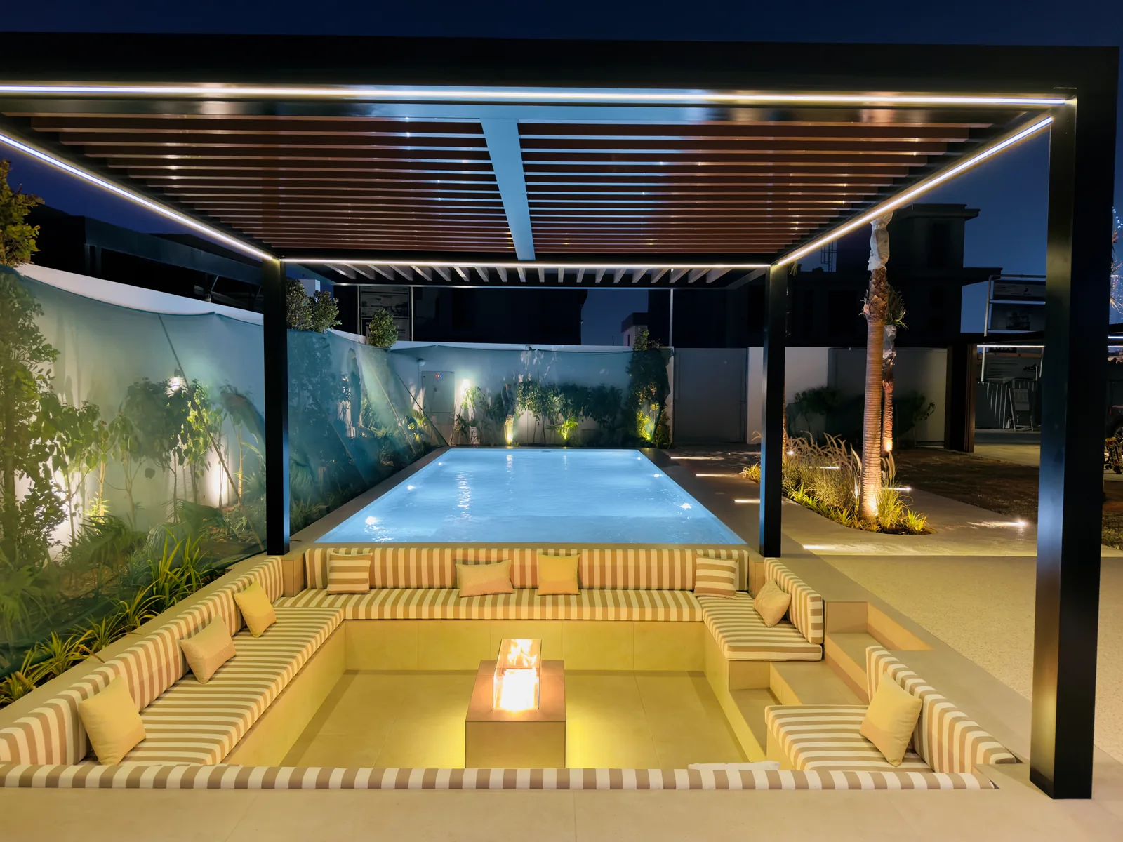 Illuminated swimming pool with sunken seating and a pergola at night